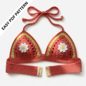 May include: A coral-colored crochet bikini top with a daisy applique and yellow trim. The top features a halter neck tie and a clasp closure. The text "EASY PDF PATTERN" is visible in the upper left corner.