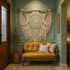 May include: A large off-white macrame wall hanging featuring a central mandala pattern and crescent moon shapes, suspended from a natural wooden branch. The intricate knotted cord design includes long fringe tassels hanging from the bottom edge.