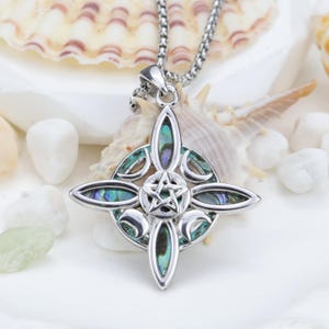 May include: A silver pendant necklace with a four-pointed design, incorporating iridescent abalone shell inlays. The centre features a pentagram. The necklace is displayed on a white surface with seashells.