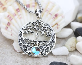 May include: A silver-toned circular pendant featuring an intricate tree of life design with exposed roots. The base of the tree is accented by a small, iridescent round cabochon stone, flanked by two crescent moon shapes on a silver chain necklace.