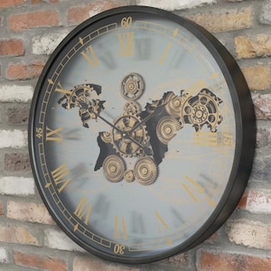 May include: A large, round wall clock with a black frame and a grey face. The clock features gold Roman numerals and a detailed world map design with gears. The clock is mounted on a brick wall.