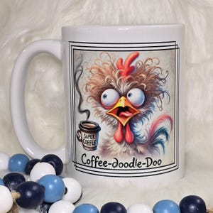 May include: White ceramic coffee mug featuring a cartoon rooster with wide eyes and a surprised expression. The rooster is holding a coffee cup with the words "Super Coffee." The mug also has the text "Coffee-doodle-Doo."