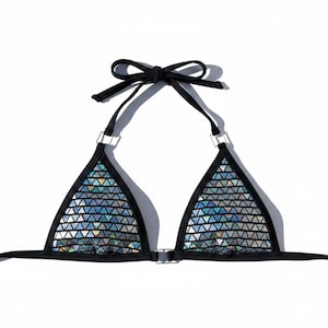 Puede incluir: Top de bikini negro con diseño de triángulo. El top presenta un patrón plateado iridiscente de pequeños triángulos. Las correas y los lazos son negros, con detalles metálicos plateados en la parte superior de cada copa triangular.