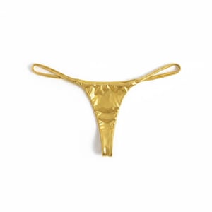Puede incluir: Bragas de tanga doradas con tirantes finos. La tela brillante y metálica refleja la luz, creando una apariencia brillante. La prenda está sobre un fondo blanco liso.