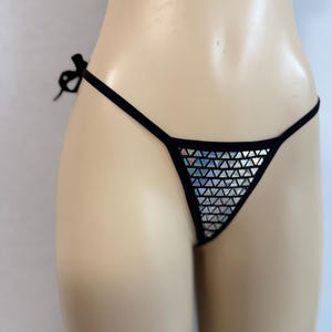 May include: Black thong bikini bottom with a triangle front panel covered in silver geometric shapes. The bikini has thin black straps that tie at the sides. The garment is displayed on a mannequin.