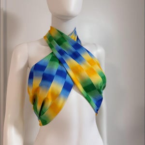 May include: A colorful halter top in shades of blue, green, and yellow. The fabric is draped and crisscrossed across the chest. The top is displayed on a white mannequin.