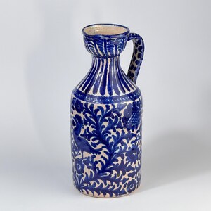Puede incluir: Jarra de cerámica azul y blanca con asa. La jarra presenta un diseño floral y de pájaros detallado. El asa tiene un patrón de puntos. La parte superior de la jarra tiene una amplia abertura. Decorada con pintura azul.