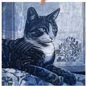 May include: A black and white cat with green eyes is lying on a blue and white patterned cushion, looking out a window. The cat is in a relaxed pose, with its head tilted slightly to the side. The window is open, and there are some flowers outside.