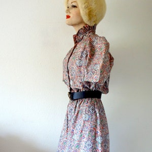 May include: A vintage dress with a paisley print in shades of red, blue, and white. The dress has a collared neckline, long sleeves, and a fitted waist with a black belt.
