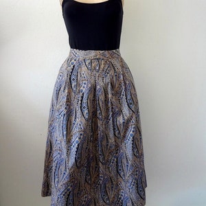May include: A midi-length skirt with a paisley print in shades of blue, brown, and white. The skirt has a fitted waist and a flowing, A-line silhouette.