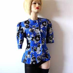 Op de afbeelding: Een blauw en wit bloemenprint jack met een getailleerde pasvorm en driekwart mouwen. Het jack wordt gedragen door een mannequin met een witte bontmuts.