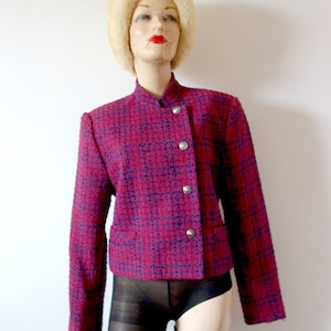 Pode incluir: Um blazer de tweed rosa e azul com um fecho de botão único. O blazer tem colarinho e mangas compridas.