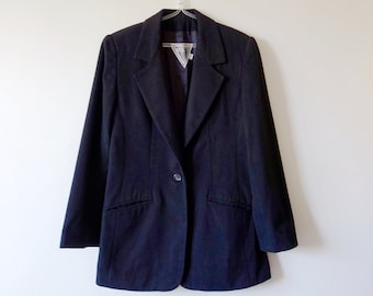 May include: A black blazer with a single button closure and two pockets. The blazer is hanging on a white hanger against a white wall.