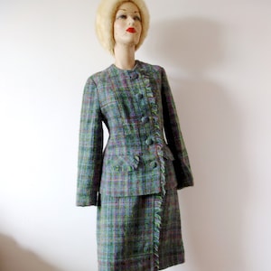 Pode incluir: Um conjunto de saia e blazer xadrez verde, azul e rosa com detalhe de franja. O blazer tem um fecho de botão único e a saia é de comprimento até ao joelho.