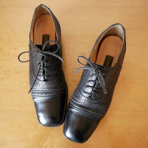 May include: A pair of black leather lace-up shoes with a perforated design. The shoes have a square toe and a low heel.
