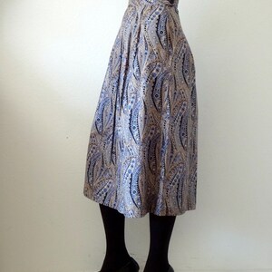 May include: A pleated midi skirt with a paisley pattern in shades of blue, brown, and white. The skirt has a high waist and a button closure.