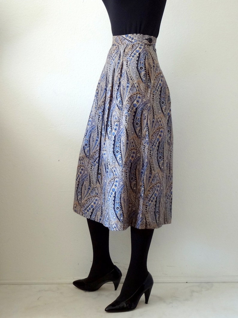 May include: A pleated midi skirt with a paisley pattern in shades of blue, brown, and white. The skirt has a high waist and a button closure.