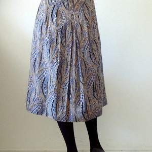 May include: A blue and gold paisley patterned skirt with a pleated design. The skirt is knee-length and has a fitted waistband.