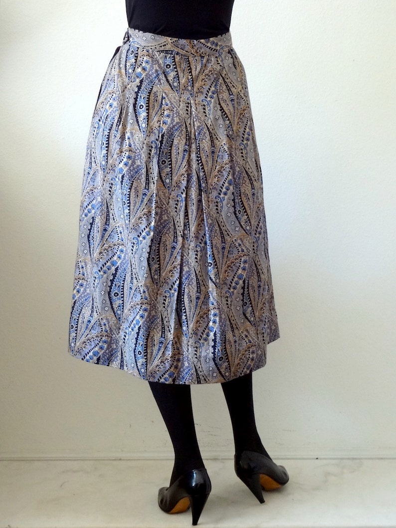 May include: A blue and gold paisley patterned skirt with a pleated design. The skirt is knee-length and has a fitted waistband.