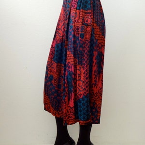 May include: A long, pleated skirt with a colorful, geometric pattern in shades of red, blue, and black. The skirt is made of a silky fabric and has a high waist.