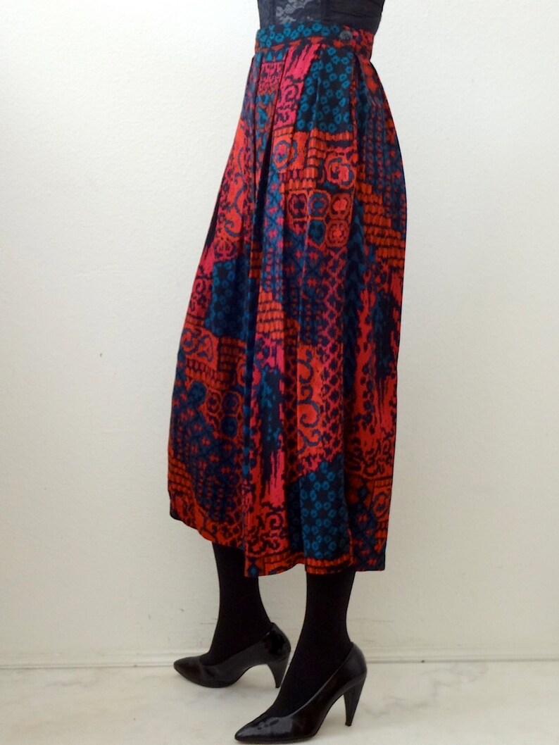May include: A long, pleated skirt with a colorful, geometric pattern in shades of red, blue, and black. The skirt is made of a silky fabric and has a high waist.