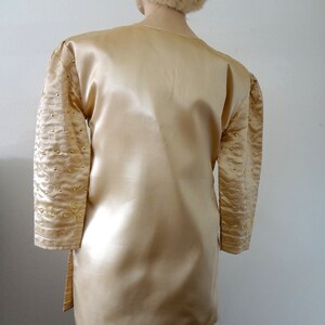 Peut inclure: Une tunique en satin dor&eacute; &agrave; manches longues. Les manches sont orn&eacute;es de broderies dor&eacute;es et de petites perles dor&eacute;es. La tunique est assortie d'un chapeau de fourrure assorti. Le v&ecirc;tement a un design fluide et &eacute;l&eacute;gant.
