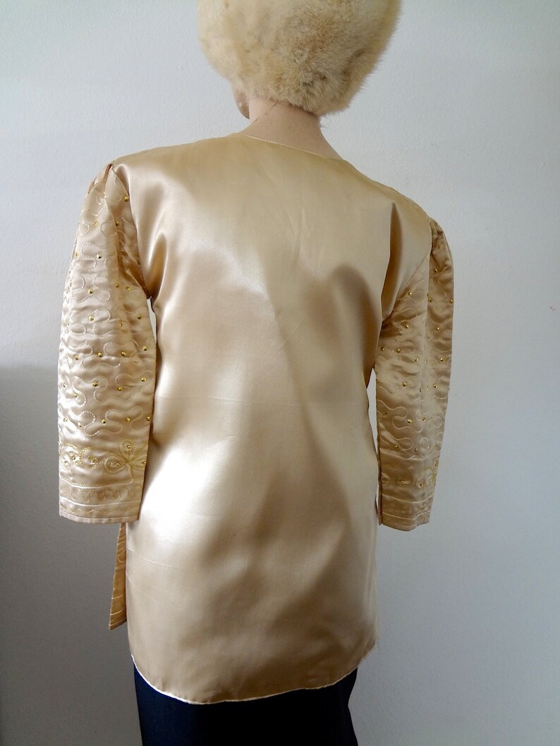 Peut inclure: Une tunique en satin dor&eacute; &agrave; manches longues. Les manches sont orn&eacute;es de broderies dor&eacute;es et de petites perles dor&eacute;es. La tunique est assortie d'un chapeau de fourrure assorti. Le v&ecirc;tement a un design fluide et &eacute;l&eacute;gant.