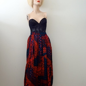 May include: A black lace bustier top paired with a red and blue patterned skirt. The skirt has a geometric design and is knee-length.