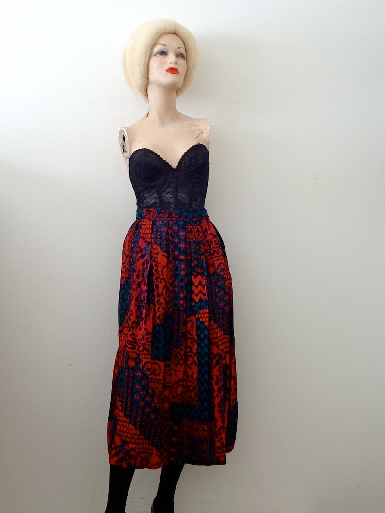 May include: A black lace bustier top paired with a red and blue patterned skirt. The skirt has a geometric design and is knee-length.