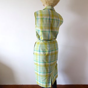 K&ouml;nnte beinhalten: Ein &auml;rmelloses Kleid mit einem gelben, wei&szlig;en und blauen Karomuster. Das Kleid hat einen taillierten Oberteil und einen Rock, der bis zu den Knien reicht. Das Kleid ist mit einem G&uuml;rtel in der Taille gebunden.