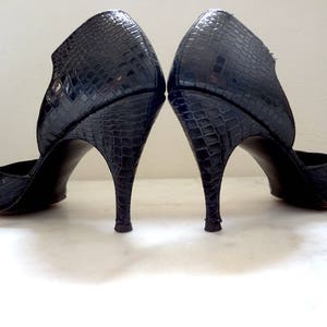 May include: A pair of black high-heeled shoes with a snakeskin pattern. The shoes have a pointed toe and a thin heel.