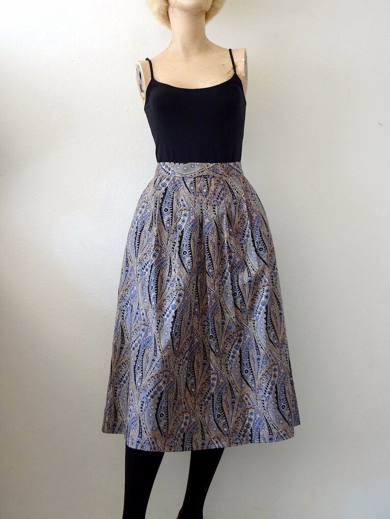 May include: A midi-length skirt with a paisley print in shades of blue, brown, and white. The skirt has a fitted waistband and a flowing silhouette.