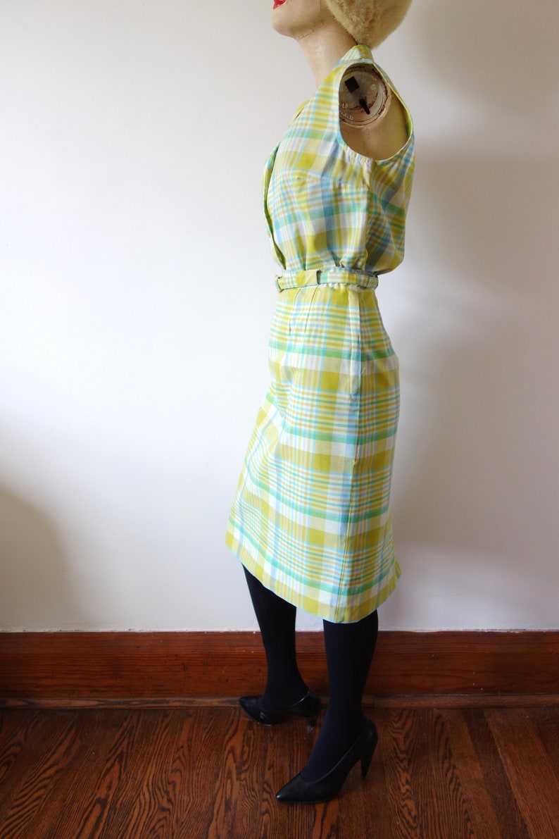 K&ouml;nnte beinhalten: Ein &auml;rmelloses Kleid mit einem gelben, gr&uuml;nen und wei&szlig;en Karomuster. Das Kleid hat einen G&uuml;rtel und eine figurbetonte Silhouette.