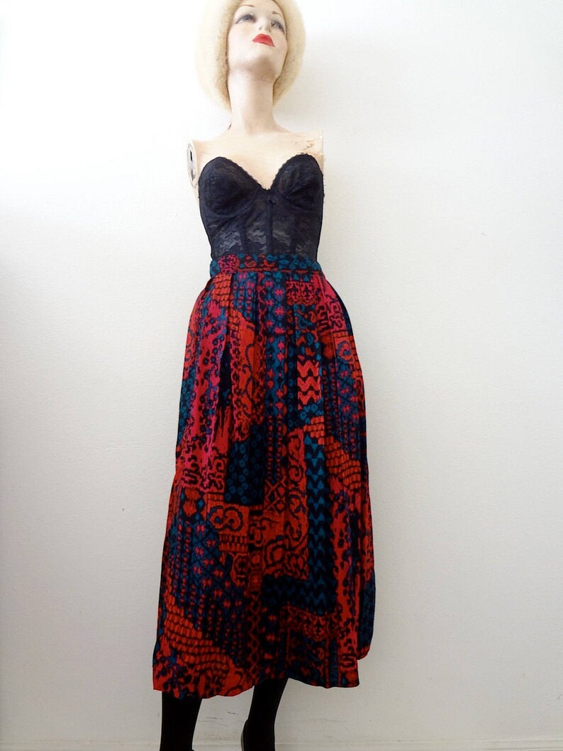 May include: A long, red, blue, and black patterned skirt with a high waist. The skirt is made of a silky fabric and has a pleated design.