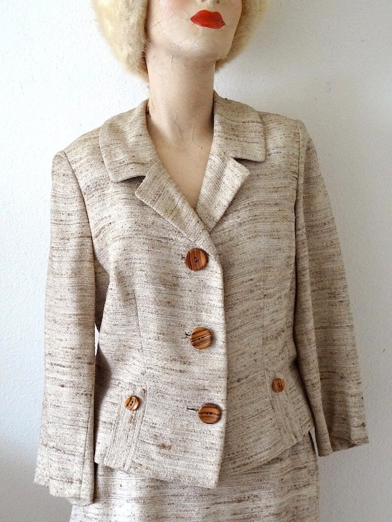 K&ouml;nnte beinhalten: Ein beigefarbener Blazer mit braunem und wei&szlig;em Streifenmuster und Holzkn&ouml;pfen. Der Blazer hat einen Kragen und Taschen.