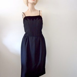 May include: A black sleeveless dress with a scalloped neckline. The dress is fitted and has a knee-length skirt.