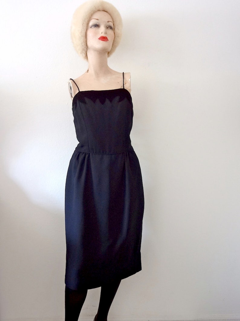 May include: A black sleeveless dress with a scalloped neckline. The dress is fitted and has a knee-length skirt.