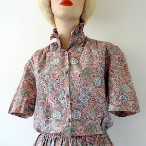May include: A short-sleeved dress with a paisley print in shades of red, blue, green, and white. The dress has a gathered waist and a ruffled collar.