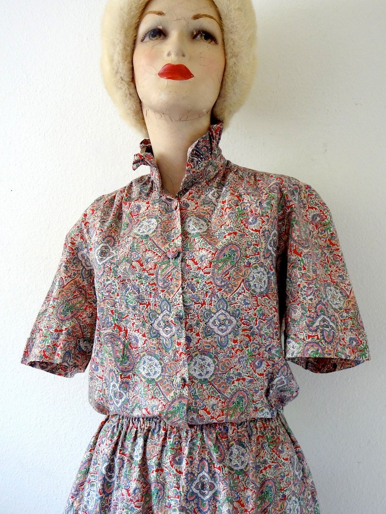 May include: A short-sleeved dress with a paisley print in shades of red, blue, green, and white. The dress has a gathered waist and a ruffled collar.