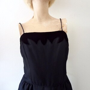May include: A black sleeveless dress with a velvet bodice and a scalloped edge. The dress has a fitted bodice and a full skirt.