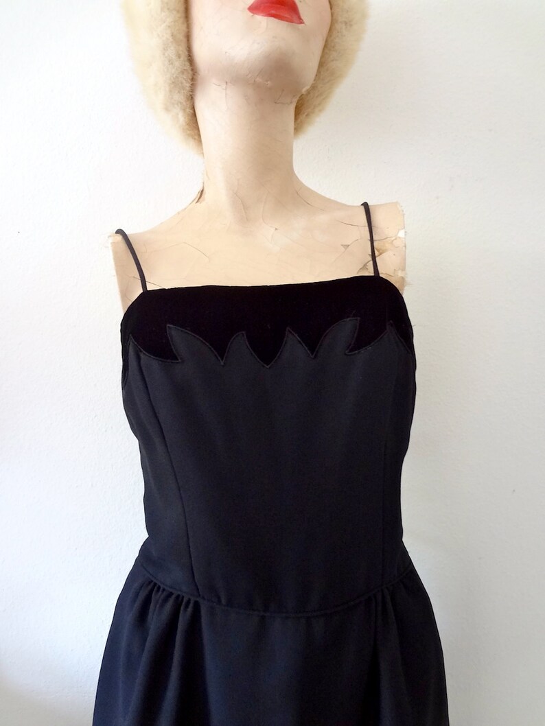 May include: A black sleeveless dress with a velvet bodice and a scalloped edge. The dress has a fitted bodice and a full skirt.