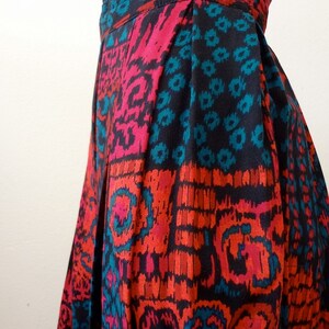 May include: A pleated skirt with a black, red, and teal geometric print. The skirt has a button closure at the waist.