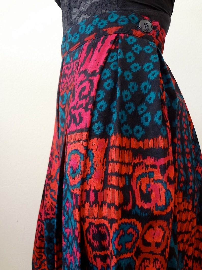 May include: A pleated skirt with a black, red, and teal geometric print. The skirt has a button closure at the waist.