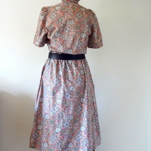 May include: A vintage dress with a paisley print and a black belt. The dress has a high collar and short sleeves.