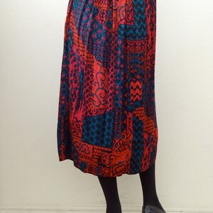 May include: A long, red, blue, and black patterned skirt with pleats. The skirt is made of a silky fabric and has a high waist.