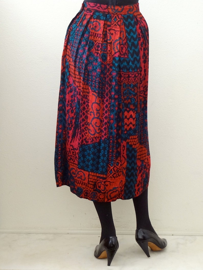 May include: A long, red, blue, and black patterned skirt with pleats. The skirt is made of a silky fabric and has a high waist.