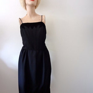 May include: A black sleeveless dress with a velvet trim around the neckline. The dress has a fitted bodice and a slightly flared skirt.