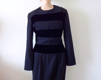 Könnte beinhalten: Ein schwarzes Kleid mit Samtbesatz und einem breiten, schwarzen Samtgürtel. Das Kleid hat lange Ärmel und eine figurbetonte Silhouette.