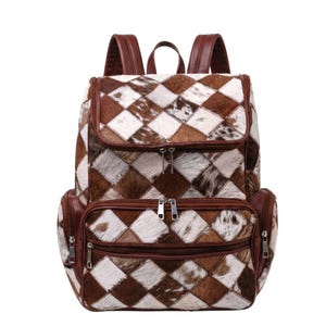 Mochila de viaje estilo western para mujer, confeccionada en piel de vaca con retazos, en tonos marrón y blanco, con pelo incrustado.