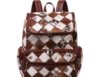 Mochila de viaje estilo western para mujer, confeccionada en piel de vaca con retazos, en tonos marrón y blanco, con pelo incrustado.